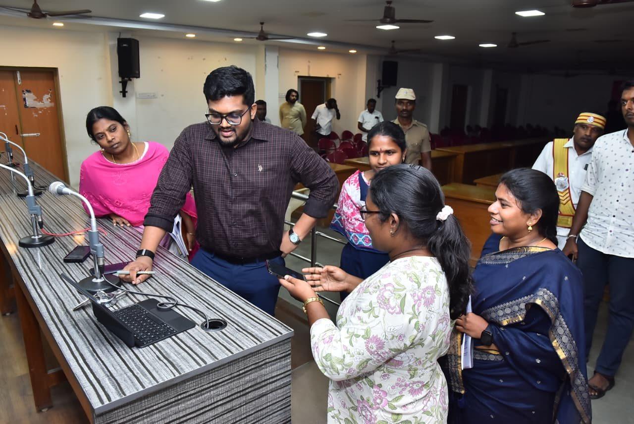 An ABOSS engineer demonstrating AlphaVoice on a phone to officials at the Tirunelveli District Collectorate, beside a conventional desk microphone